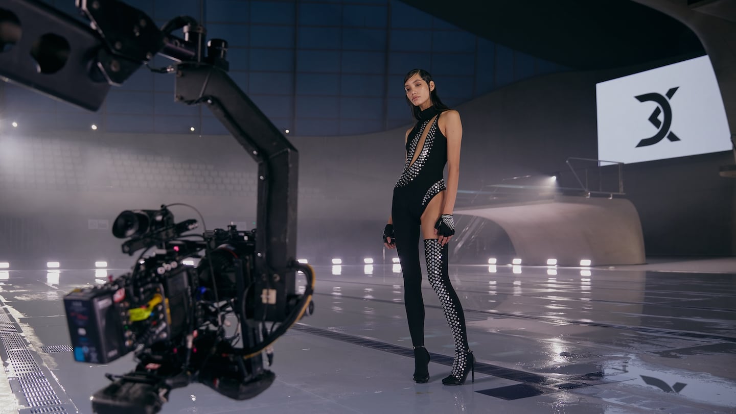 A model wears David Koma, and stands poolside in front of a video camera